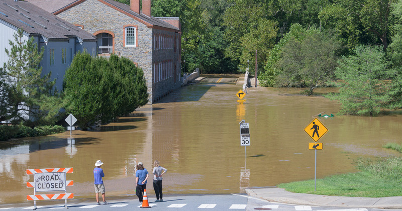 Three people standing at the edges of a flooded road