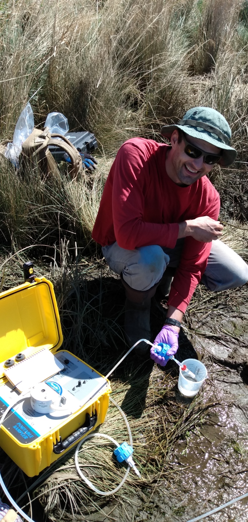 Christian squatting on the ground in a field taking samples.