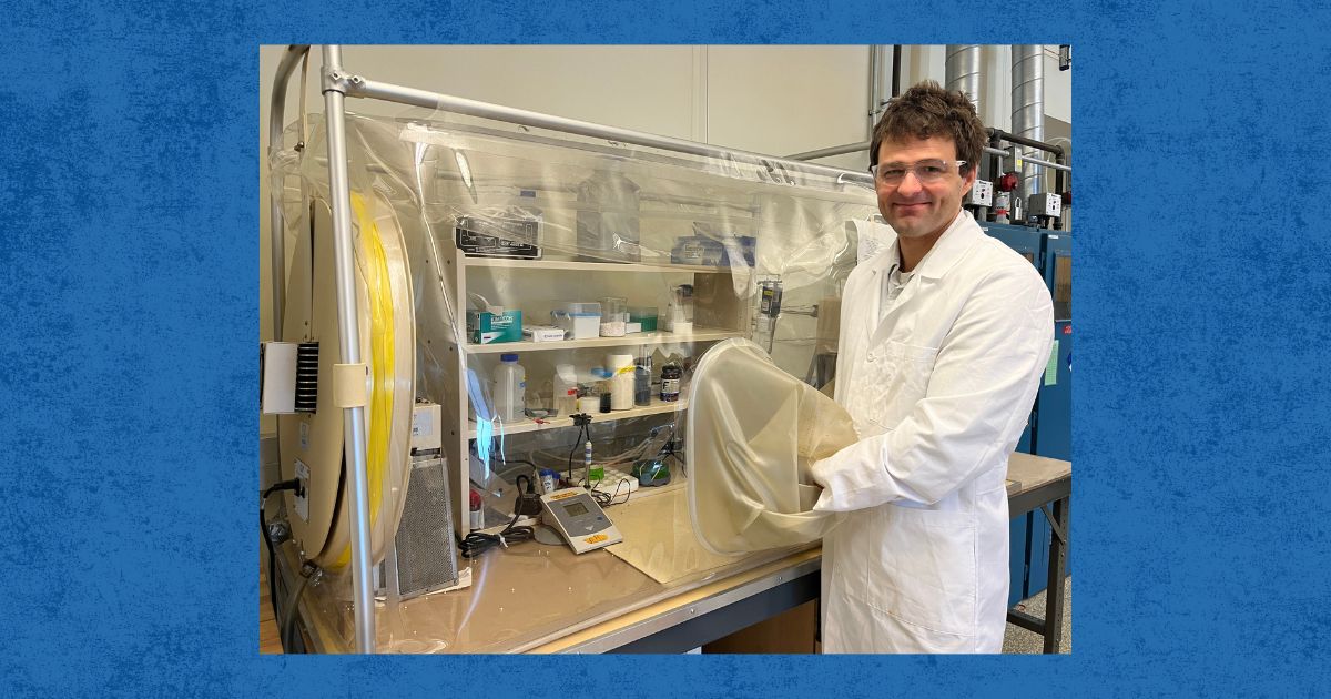 Christian Dewey stands with his hand in an anaerobic chamber, a bag that fills up mostly with nitrogen gas.