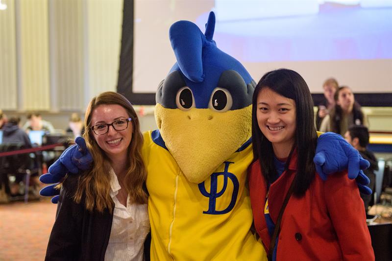 YouDee mascot with arms around two female students