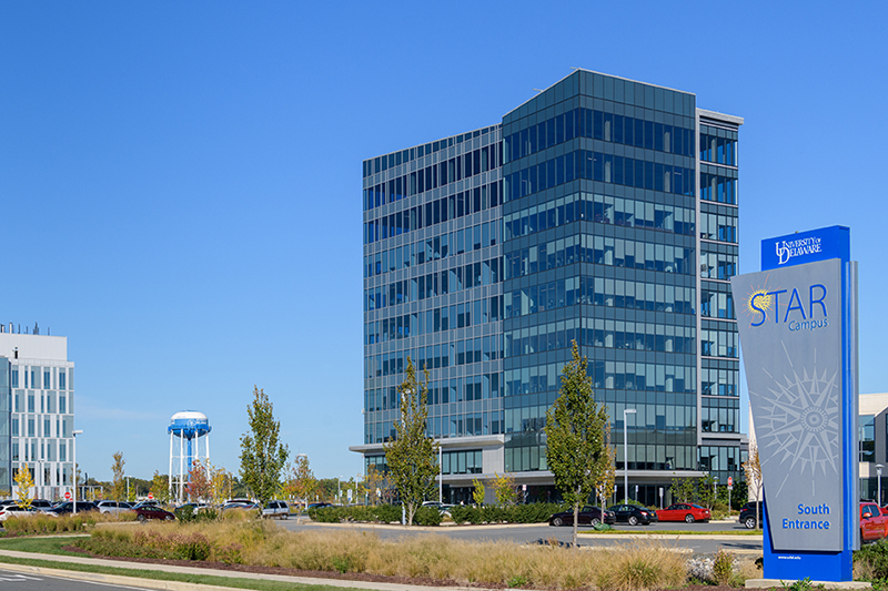 View of a glass-covered office building on a cloudless day with a sign in the foreground for the University of Delaware STAR Campus, South Entrance