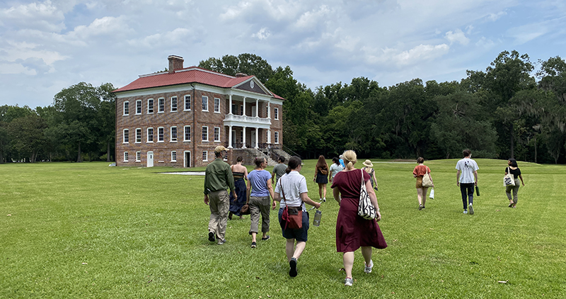 Students walking in a green field toward a historic brick house