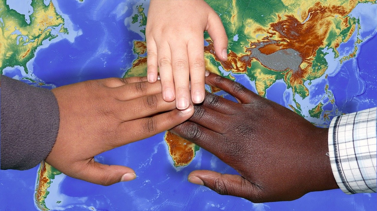 Three hands overlap each other over a map of the world