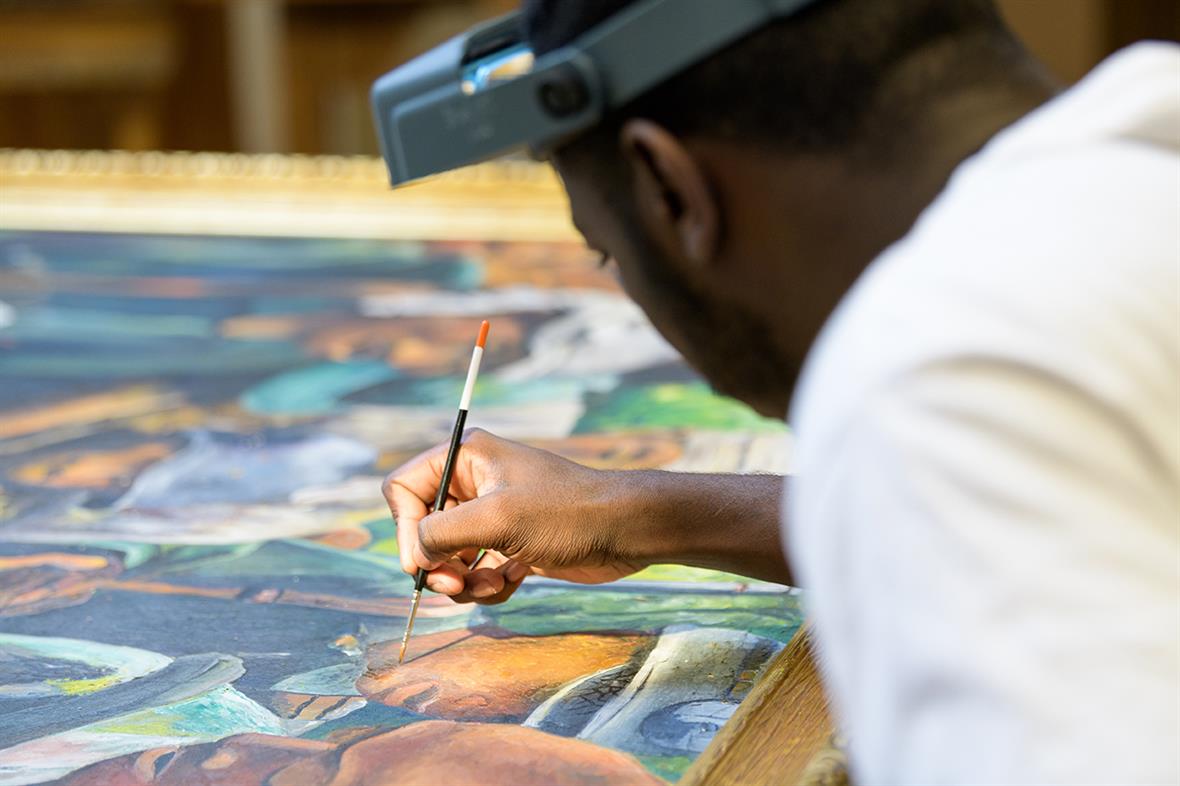 A Black male with a head-mounted magnifier working to restore a painting