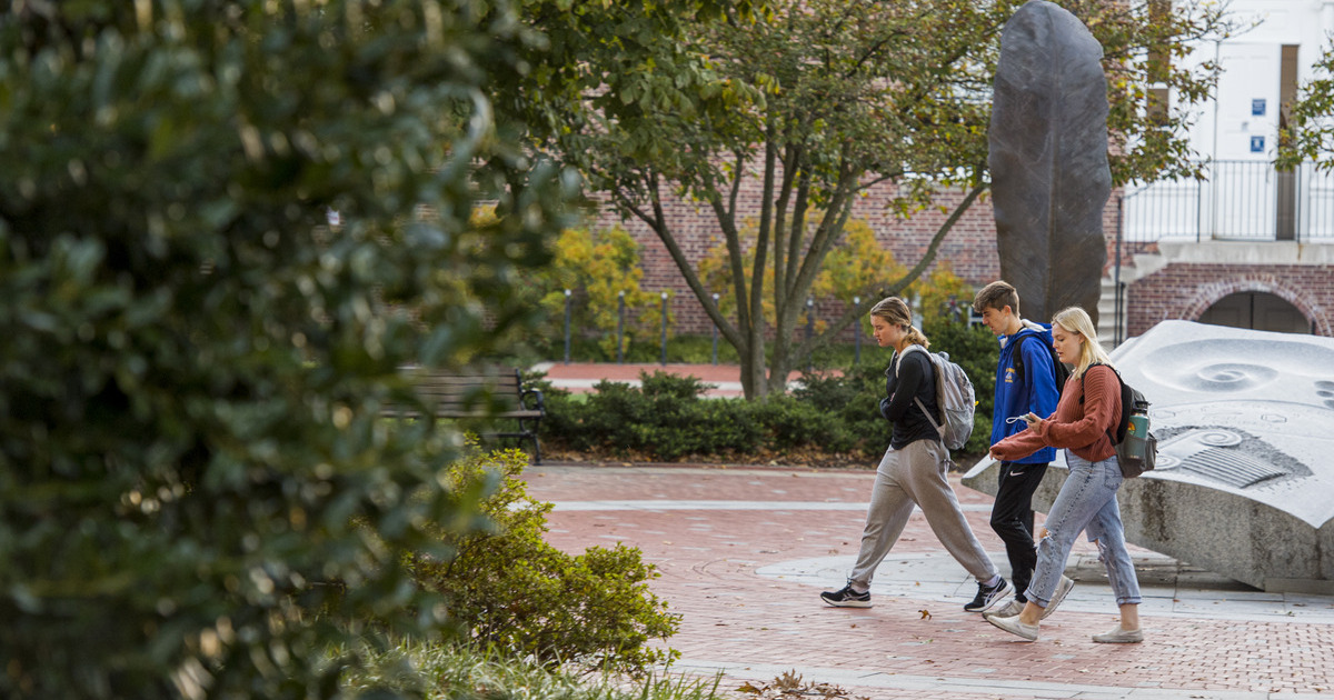 Three students walking on campus pass by Mentor's Circle at the University of Delaware in Newark.