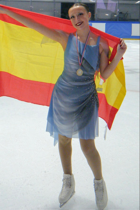 Woman is blue ice skating costume holding a red and yellow flag.