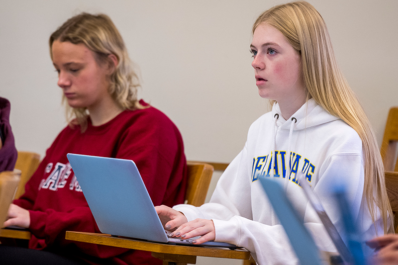 A college student, wearing a white University of Delaware sweatshirt takes notes on her laptop during a philosophy class.
