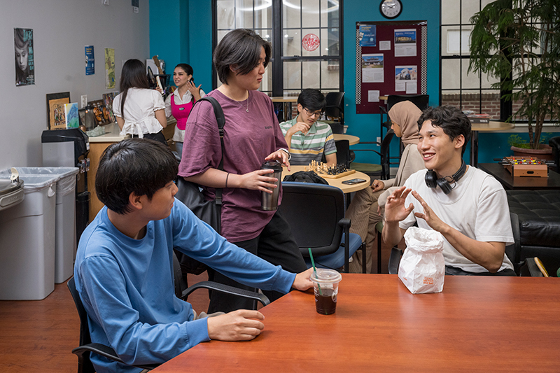 Group photo of college students gathered in a lunch room talking to each other and enjoying snacks and drinks.