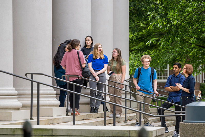 A group of University of Delaware students talk outside a historic academic hall with large white columns.