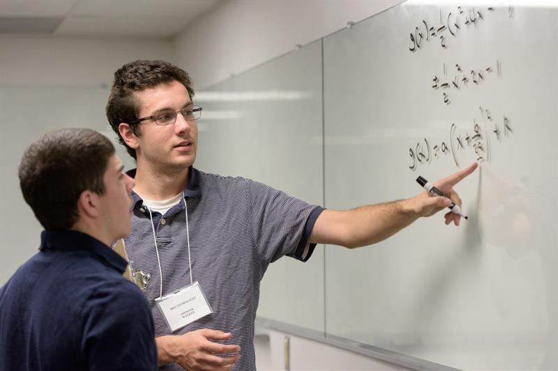 Students doing a math equation at a clear board