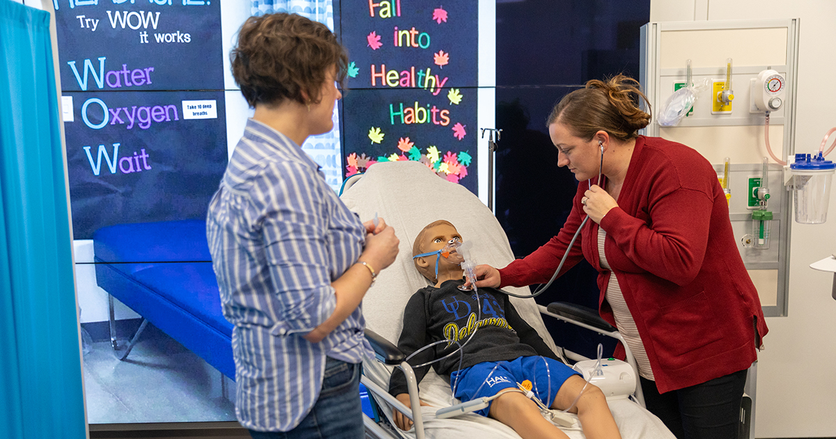 School nurses participate in a asthma exacerbation so they can sharpen their skills and be prepared for emergencies they face on the job. Shown here, a school nurse is listening to breath sounds on a high-fidelity mannequin while another school nurse watches.