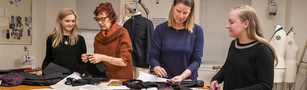 Two instructors and two students around a sewing table cutting fabric.