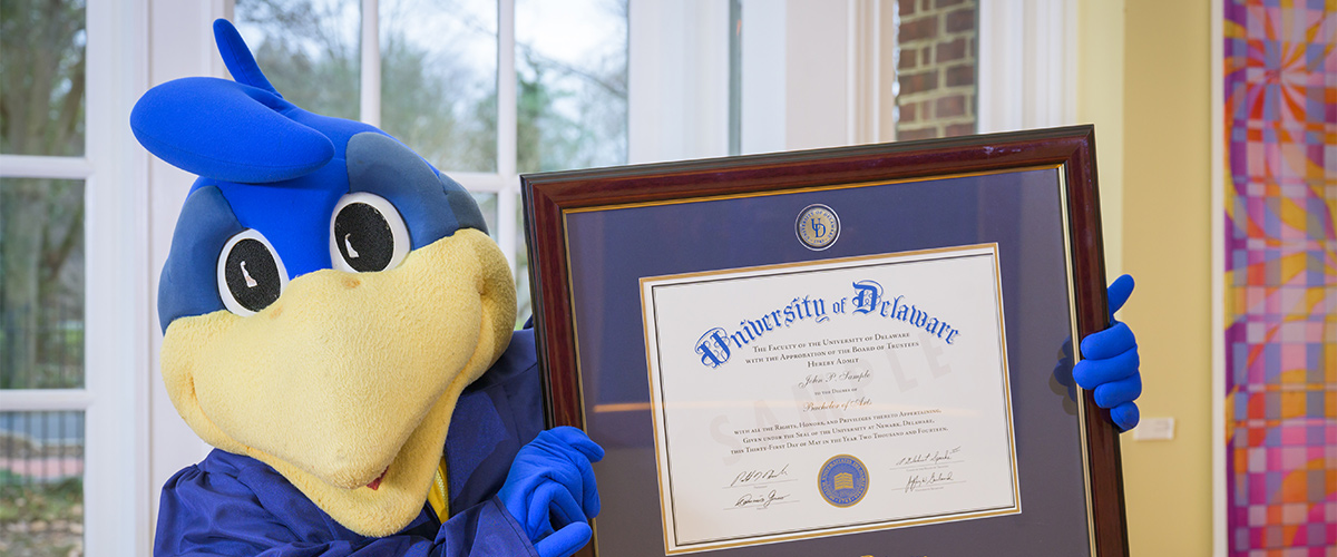 YoUDee holds up a framed "sample diploma" to the camera as if to say, "See? You can do it!"