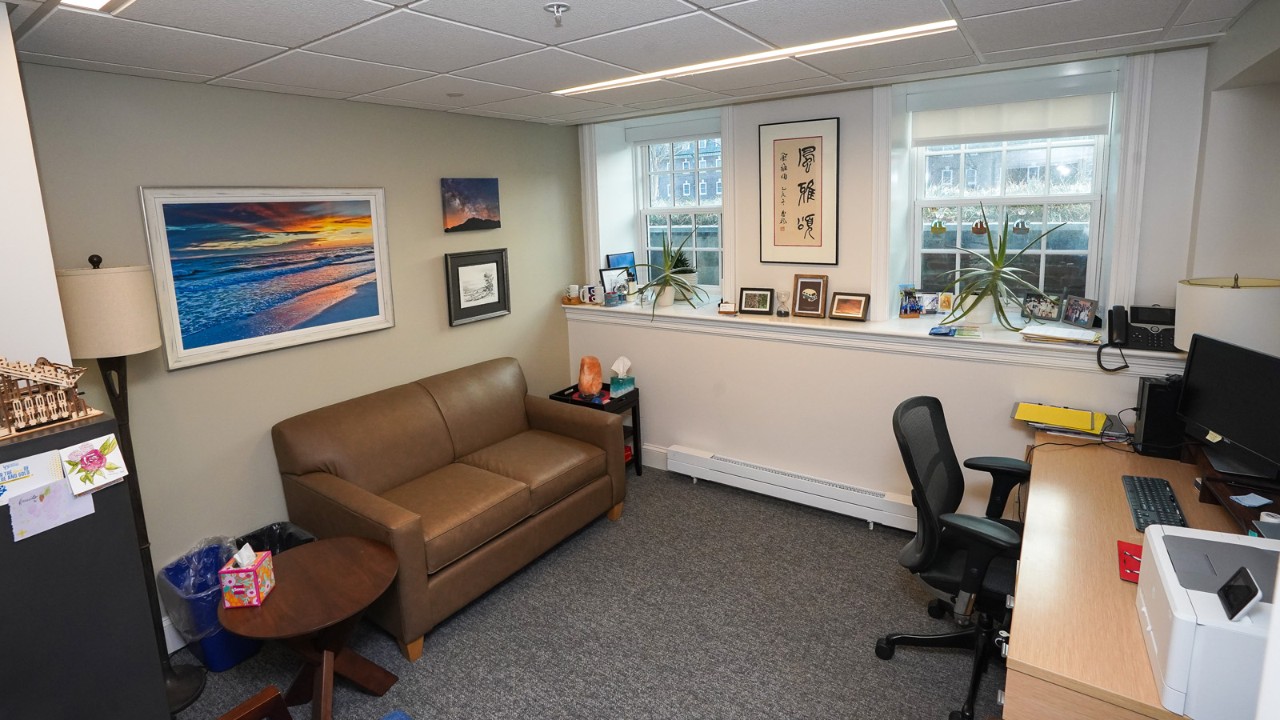 an office with a desk and chair, plus a couch beneath windows