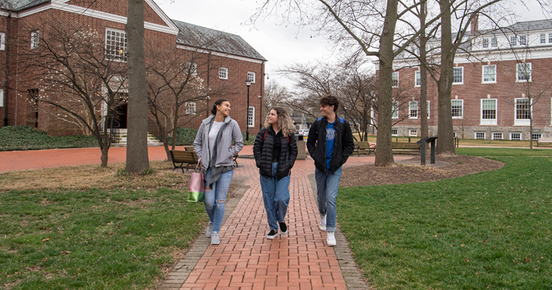 Three students walk outside Warner Hall on The Green