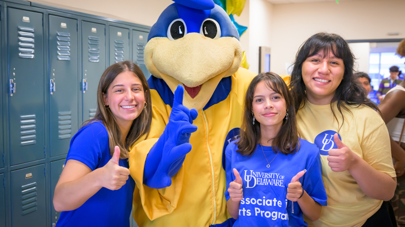 three students, one wearing a t-shirt that reads "Associate in Arts Program" pose with thumbs-up with You Dee