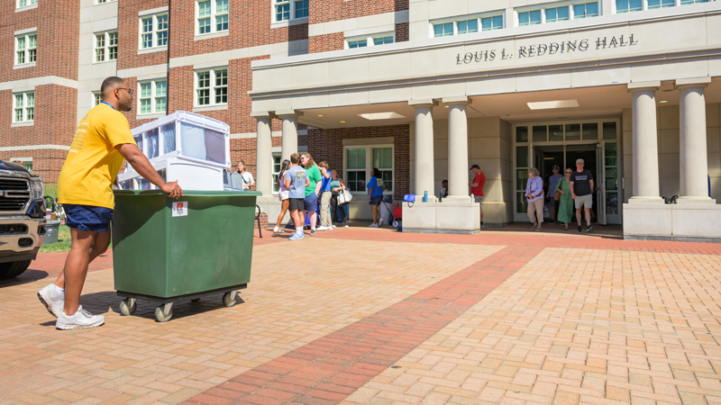 a student pushes a cart full of belongings outside a residence hall