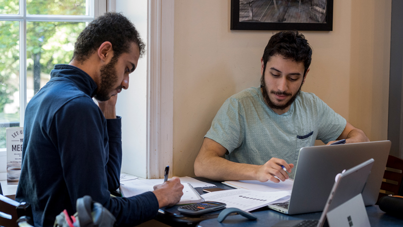 two students study at a table inside a classroom.