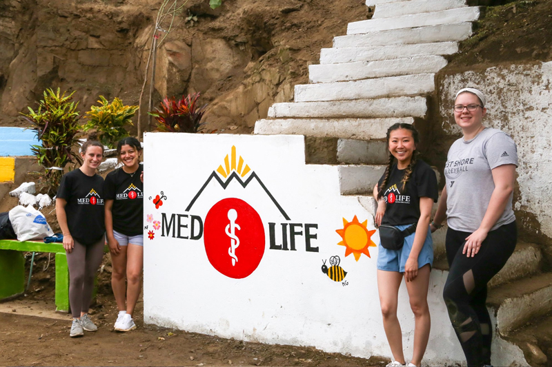 Erin Dacey, now a senior at UD, and UD alumna Abigail Flores-Toscano (on left) paint a MEDLIFE mural as part of a beautification project along with physician assistant students from Arcadia University.