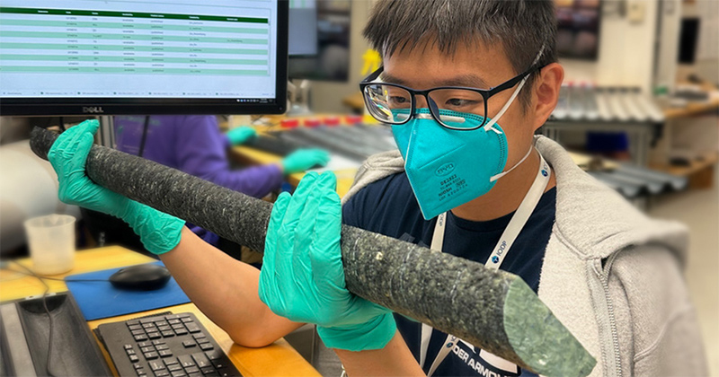 Kuan-Yu Lin, a doctoral candidate in the Department of Earth Sciences at the University of Delaware, was a recent participant on the International Ocean Discovery Program Expedition 399: Building Blocks of Life that sailed to the Atlantis Massif — an underwater mountain in the North Atlantic Ocean — to drill into and sample the Earth’s mantle. Lin is pictured here examining one of the mantle rock samples that was recovered on the cruise. For his role on the cruise, Lin worked as an igneous petrologist who described the core samples as soon as they came aboard the ship.
