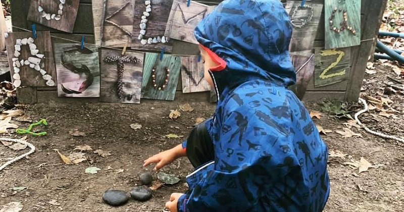 A child makes letters out of rocks during an outdoor activity at the Lab School. 