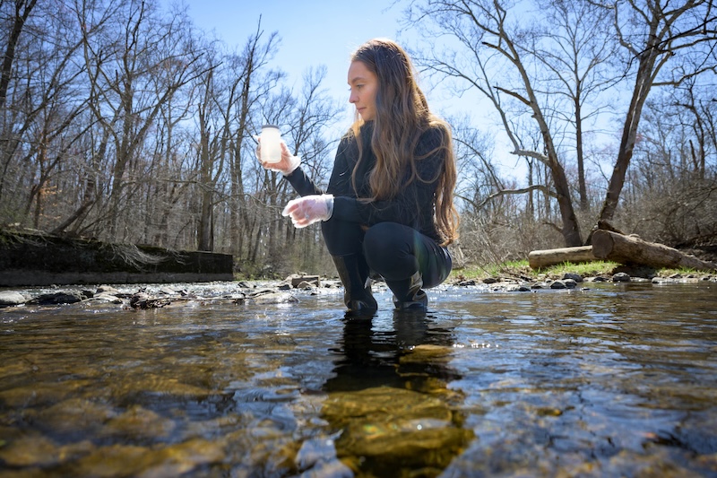 Megan Wassil, a doctoral student in water science and policy, collects water samples from a Delaware stream as part of her research examining PFAS levels in local drinking water sources.